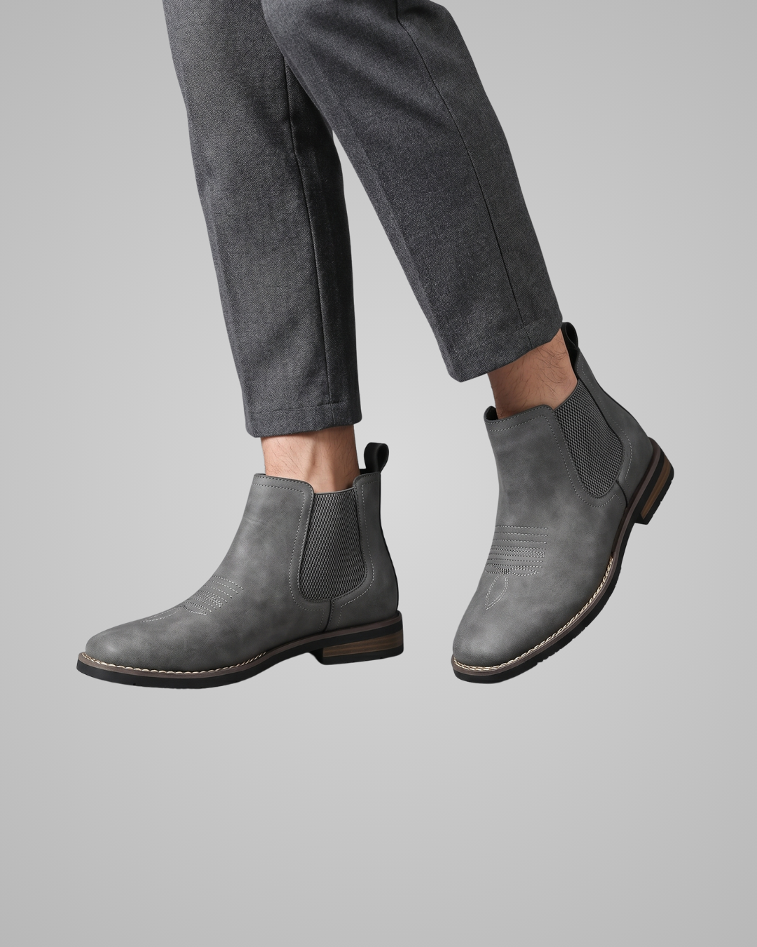 Grey leather Chelsea boots worn with navy pants on a light gray background