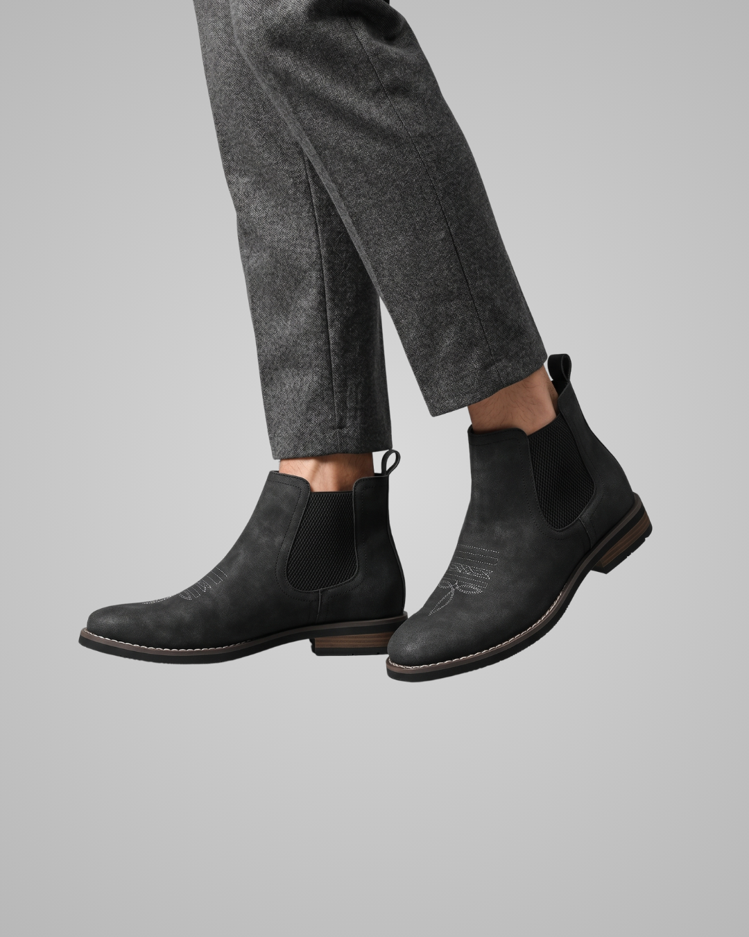 Black Chelsea boots worn with gray pants on a gray background