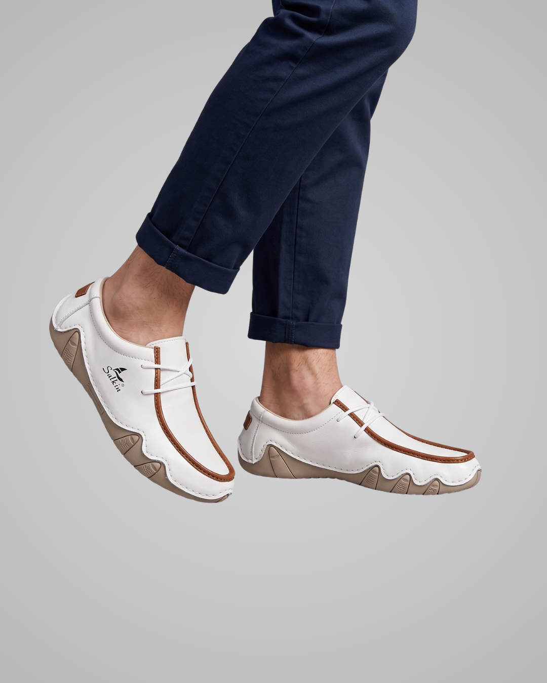 White sneakers with brown soles worn by a person on a gray background