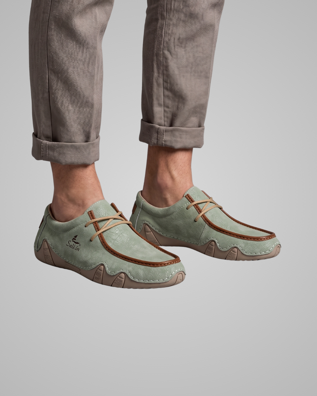 Light green loafers worn with rolled-up gray pants on a plain background
