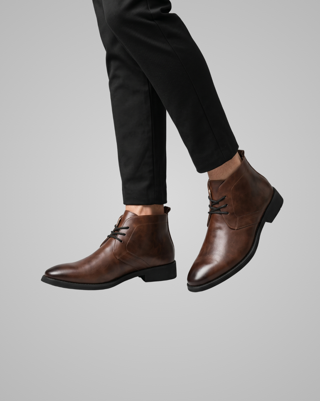 Brown leather boots worn with black pants on a gray background