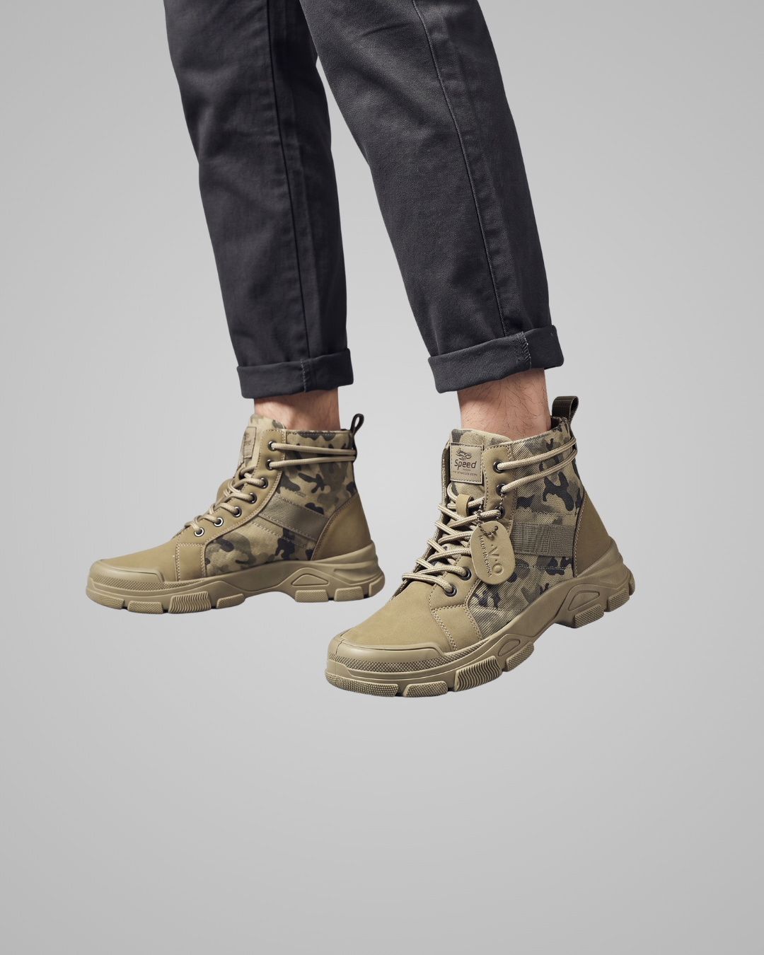Tan camouflage boots worn with black pants on a gray background