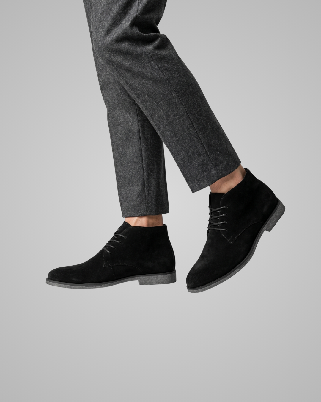 Black dress shoes worn with gray pants on a light gray background
