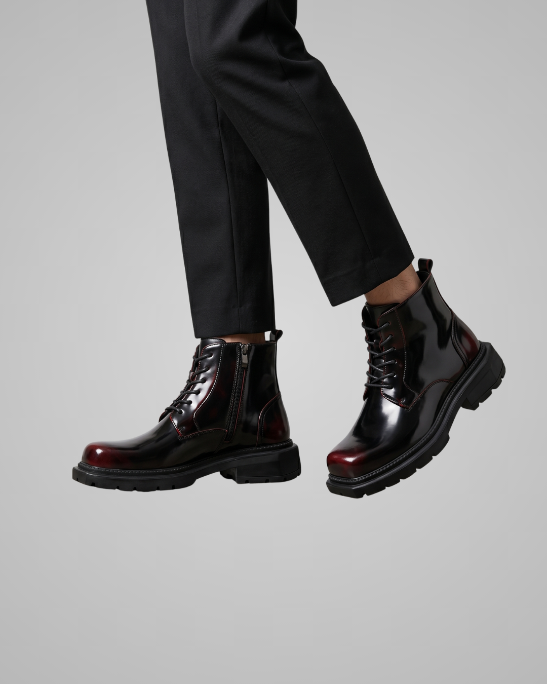 Shiny black boots with red soles on a gray background