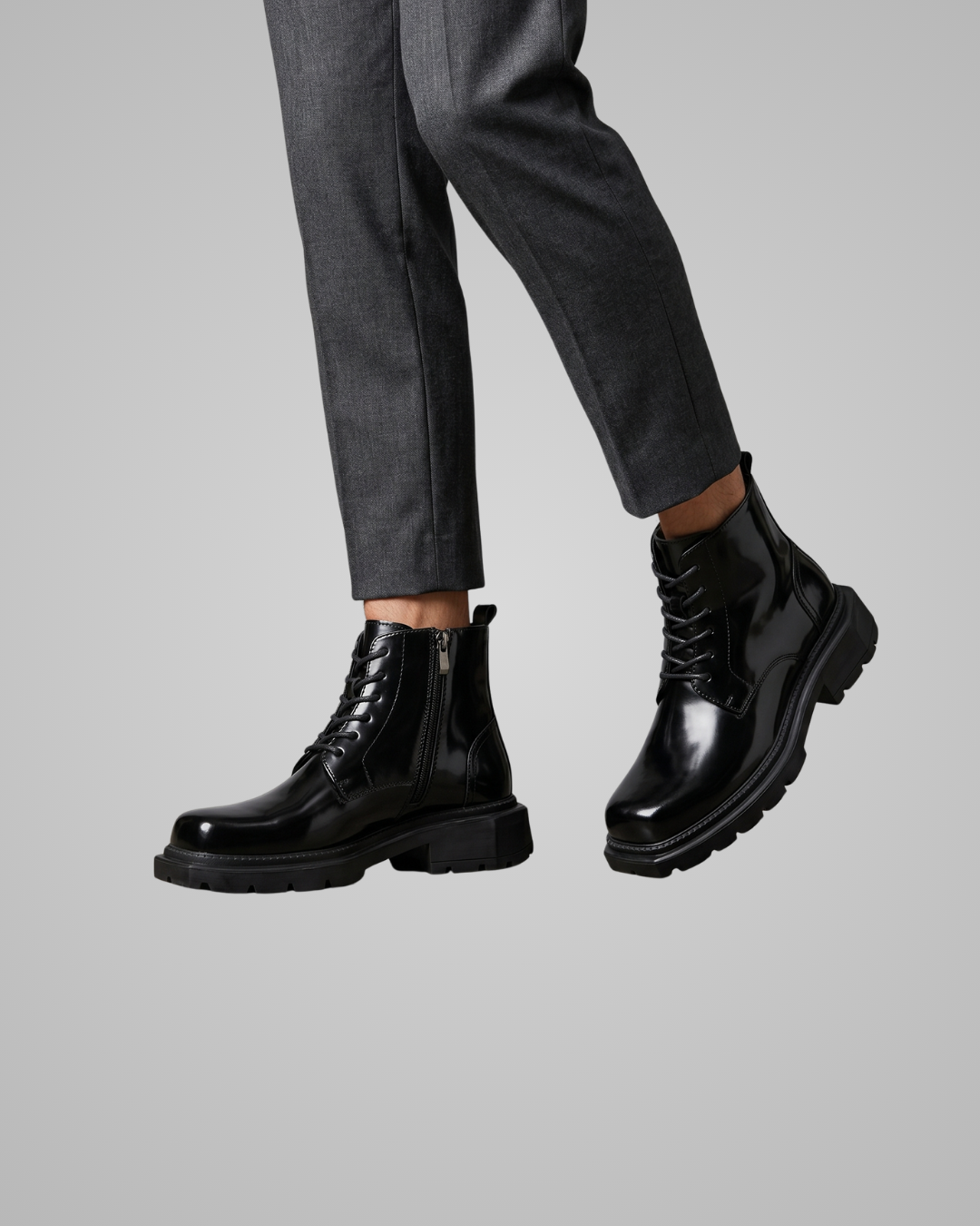 Black leather boots worn with gray pants on a light gray background