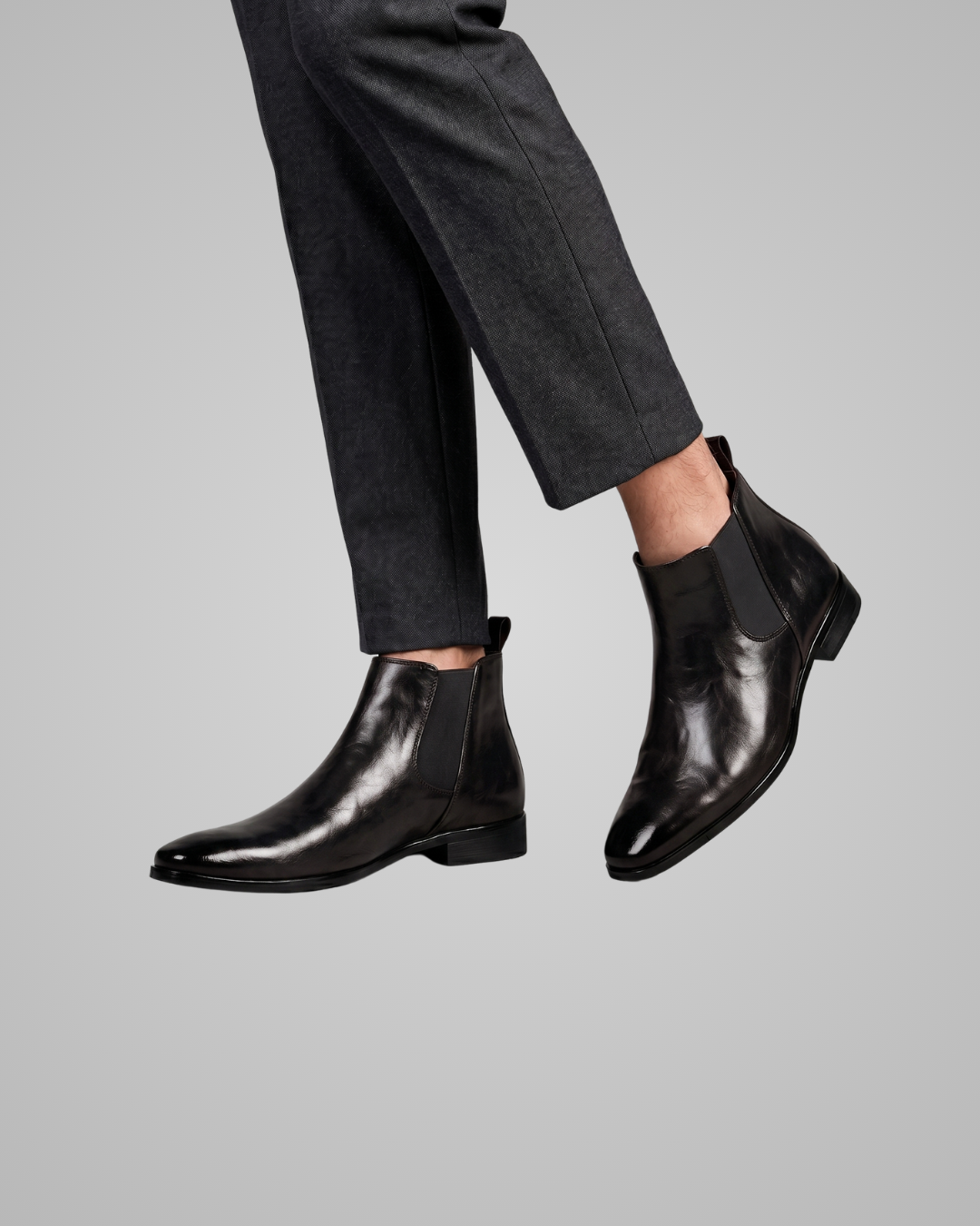 Black leather Chelsea boots worn with gray pants on a light gray background