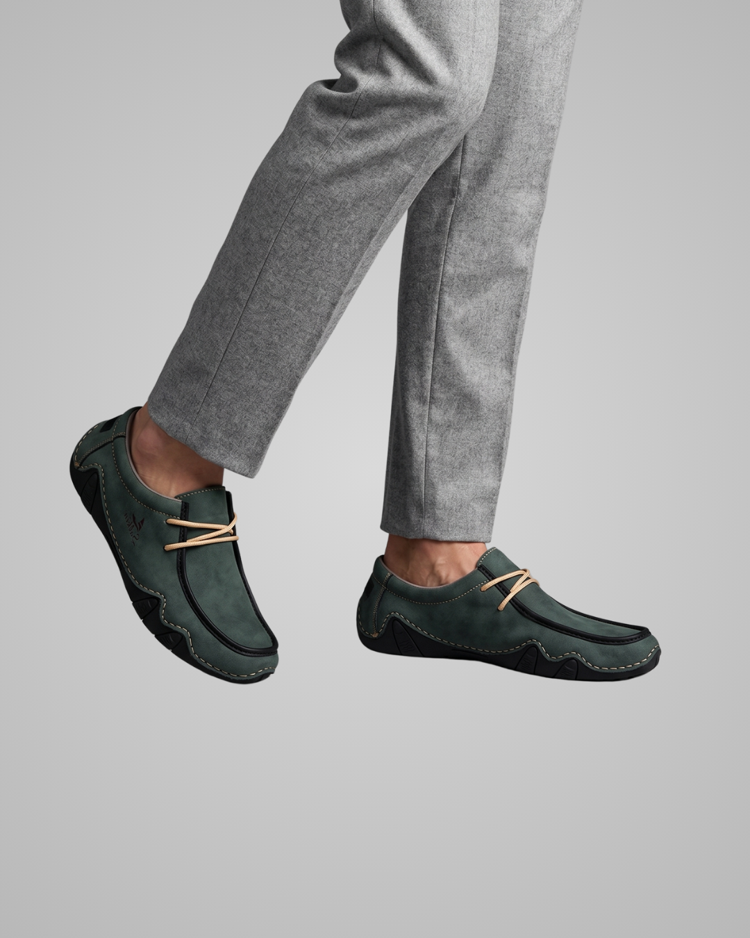 Person wearing dark green loafers with tan laces on a gray background
