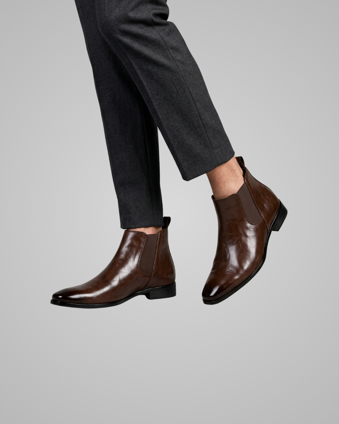 Brown leather Chelsea boots worn with gray pants on a light gray background