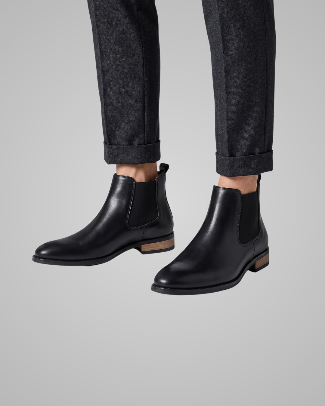 Black Chelsea boots worn with dark pants on a gray background