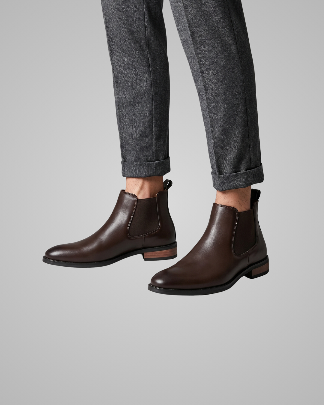 Brown leather Chelsea boots worn with gray pants on a light gray background