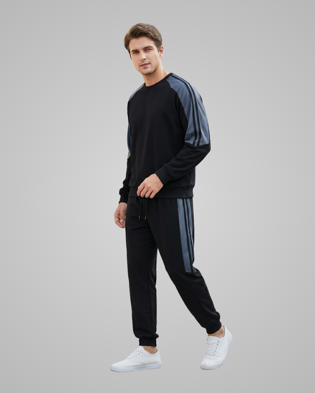 Man wearing a black and gray tracksuit with white sneakers on a gray background