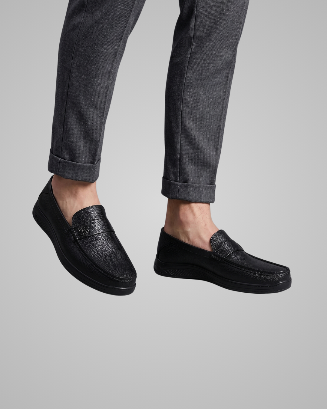 Black loafers worn with gray pants on a light gray background