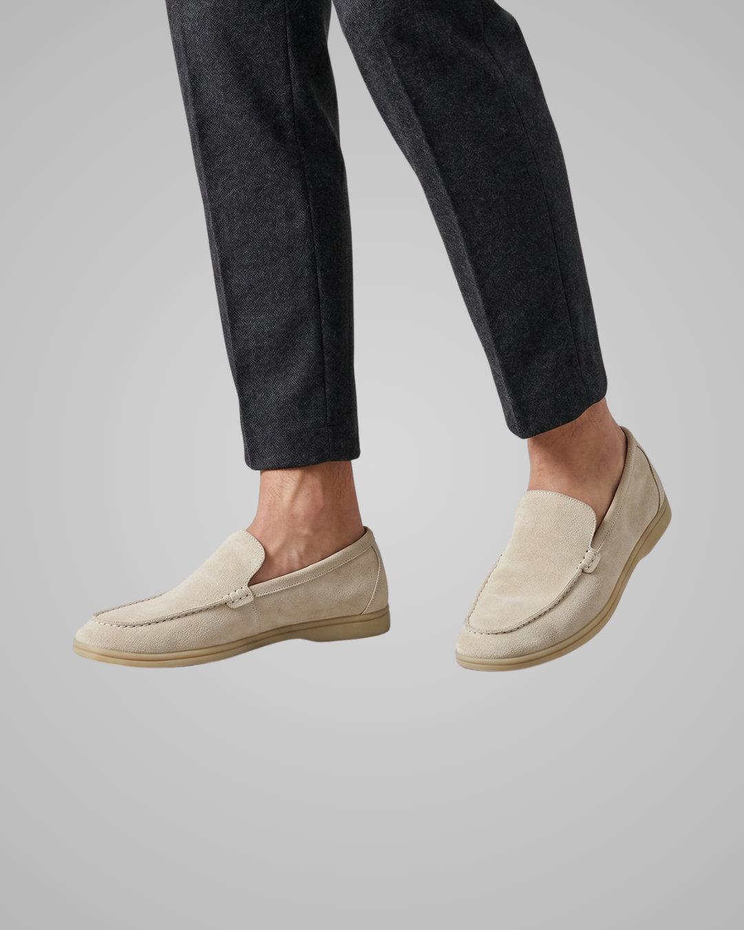 Beige loafers worn with dark jeans on a plain background