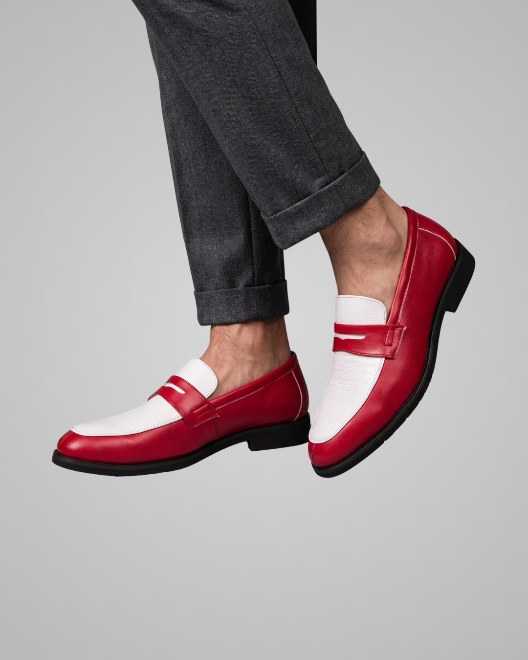 Red and white loafers worn with dark gray pants on a light gray background