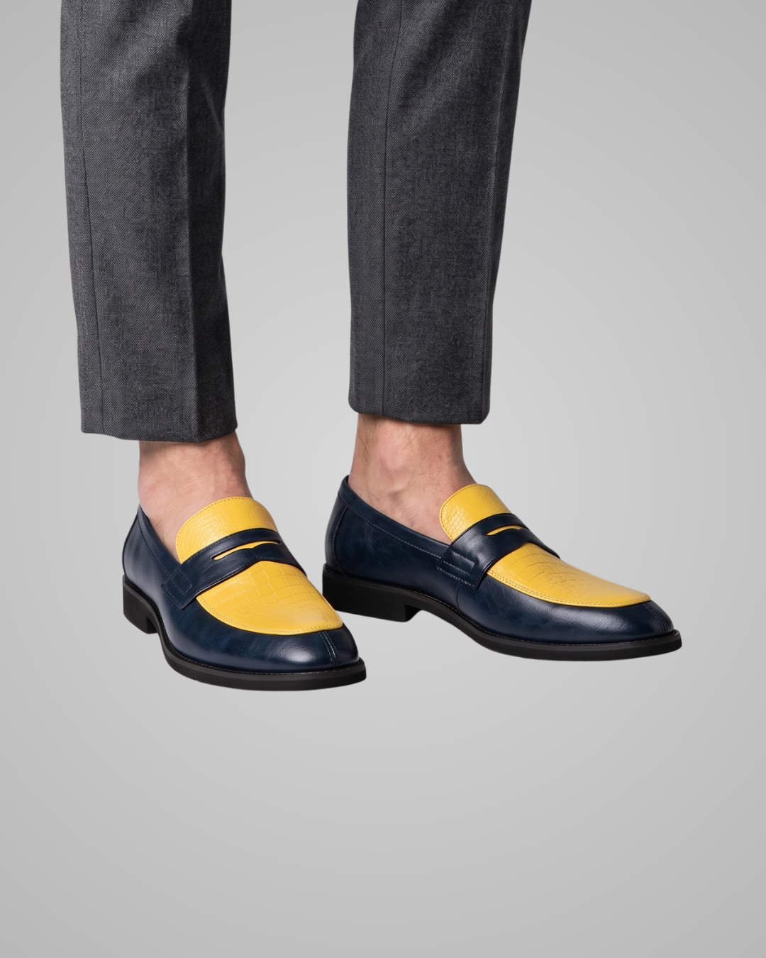 Navy and yellow loafers worn with gray pants on a light gray background