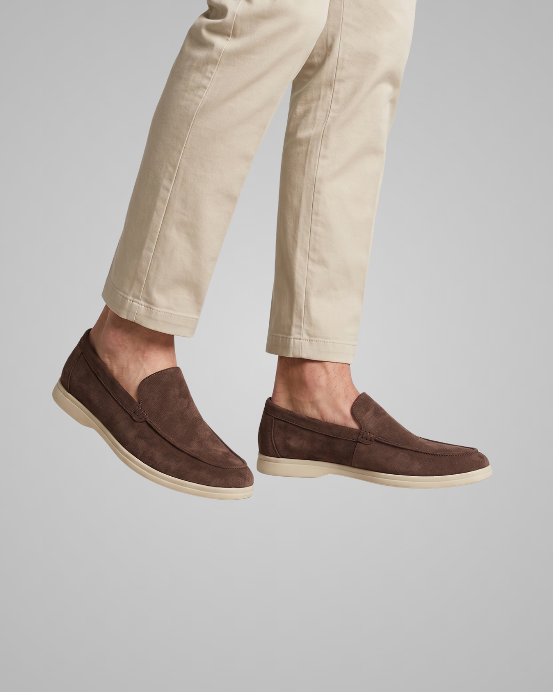 Brown loafers worn with beige pants on a gray background