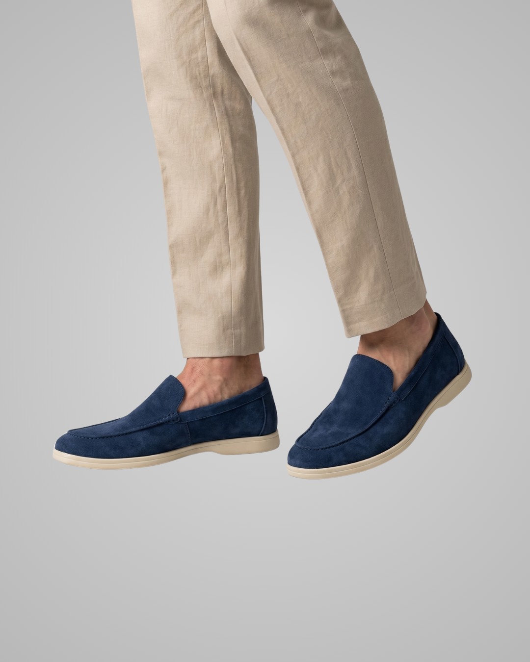 Navy loafers worn with beige pants on a gray background
