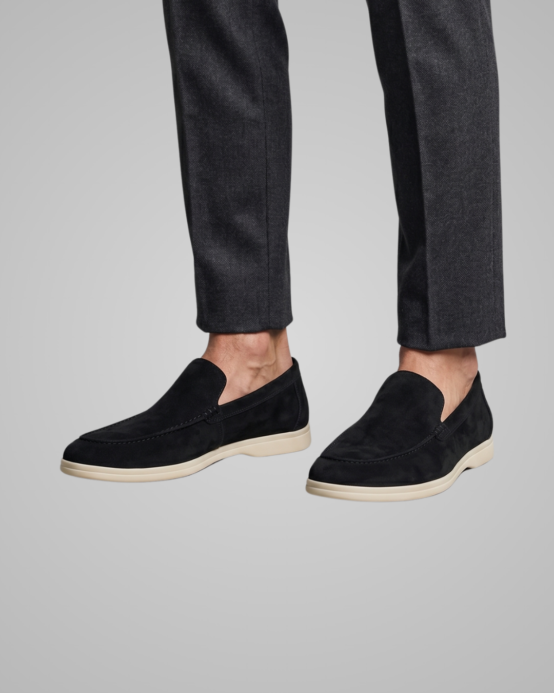 Black loafers worn with dark pants on a gray background