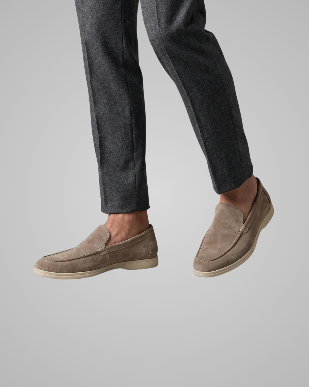 Person wearing brown suede loafers and dark gray pants on a light gray background