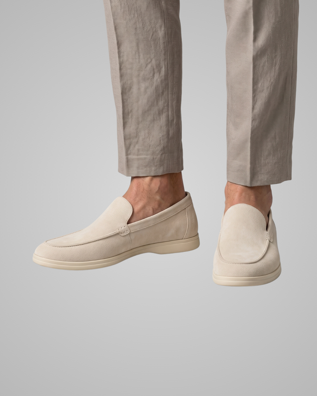 Beige loafers worn with beige pants on a plain background