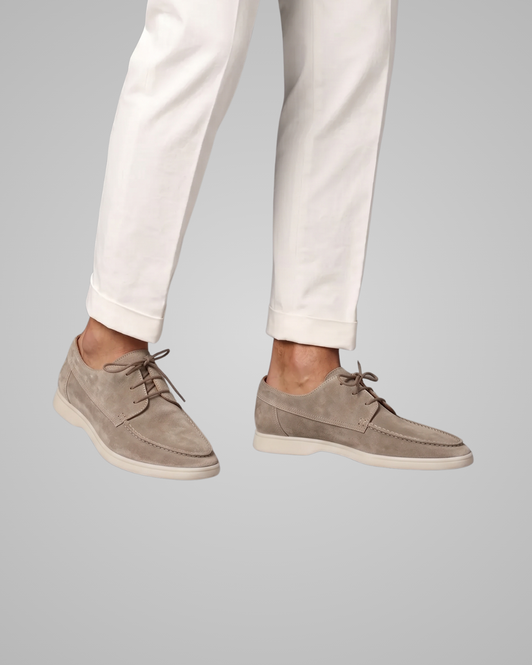 Person wearing beige suede shoes and white pants on a gray background