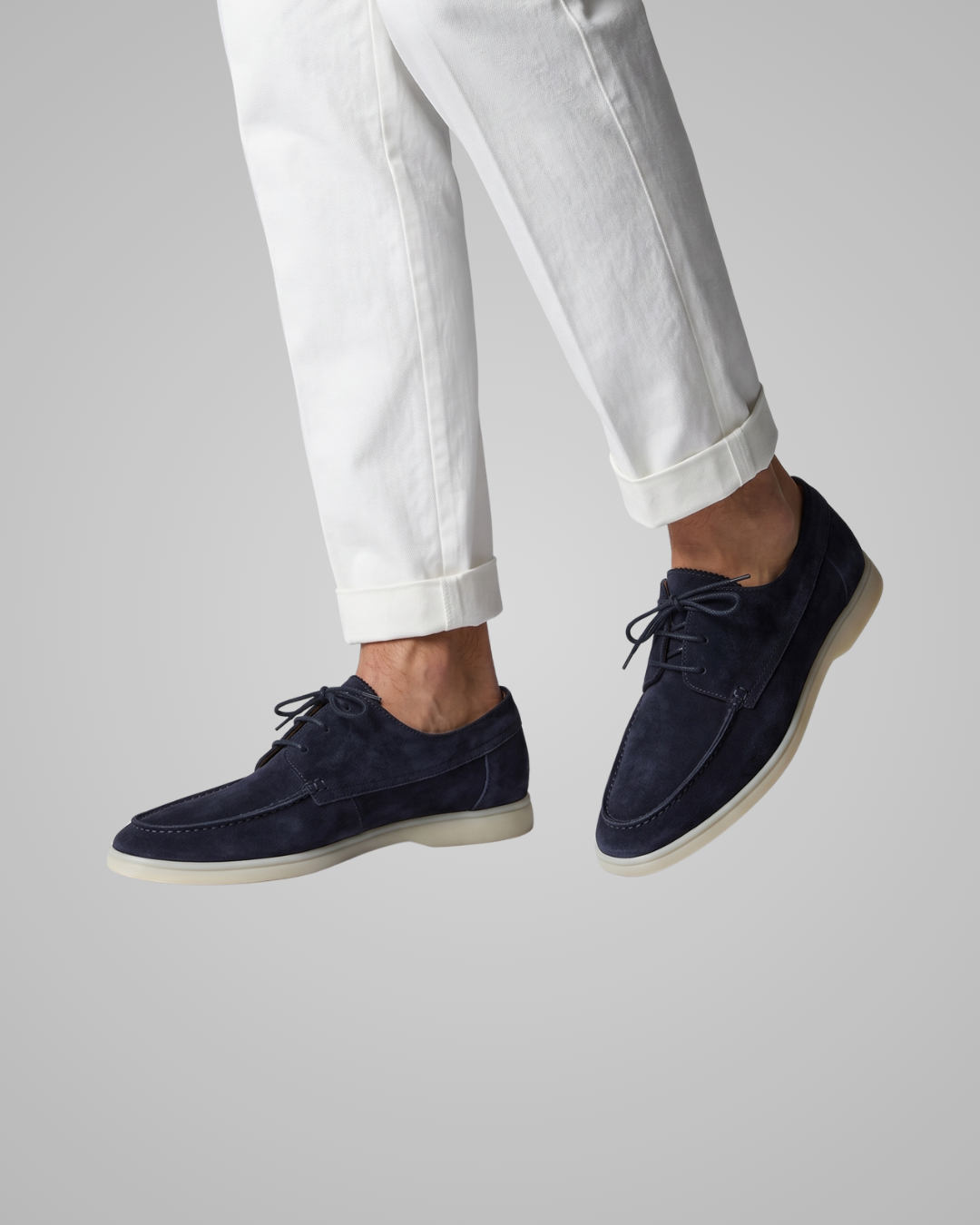 Navy suede shoes worn with white pants on a gray background