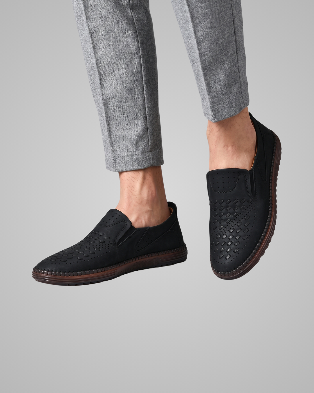 Black slip-on shoes worn with gray pants on a light gray background