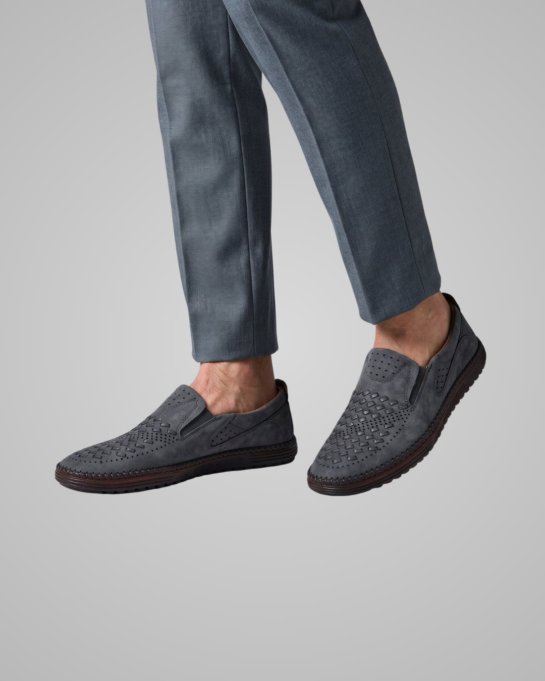 Gray loafers worn with blue pants on a gray background