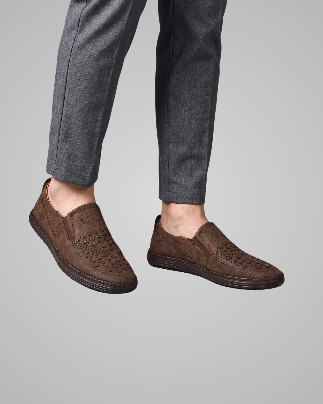 Brown loafers worn with gray pants on a gray background