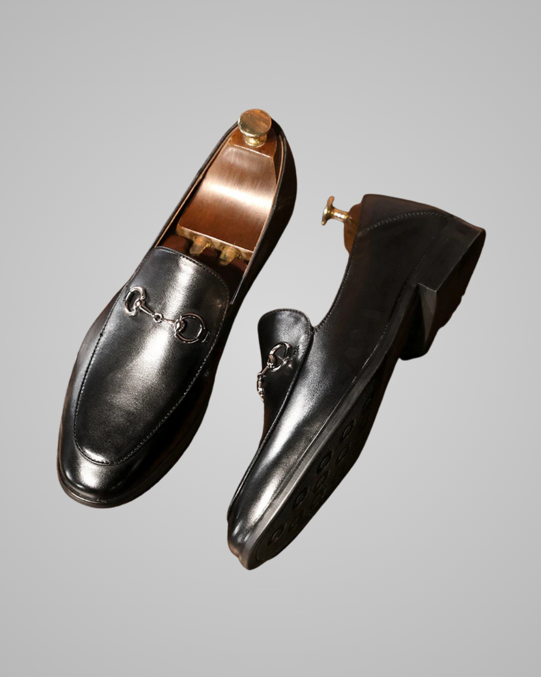 Pair of black loafers with gold accents on a gray background