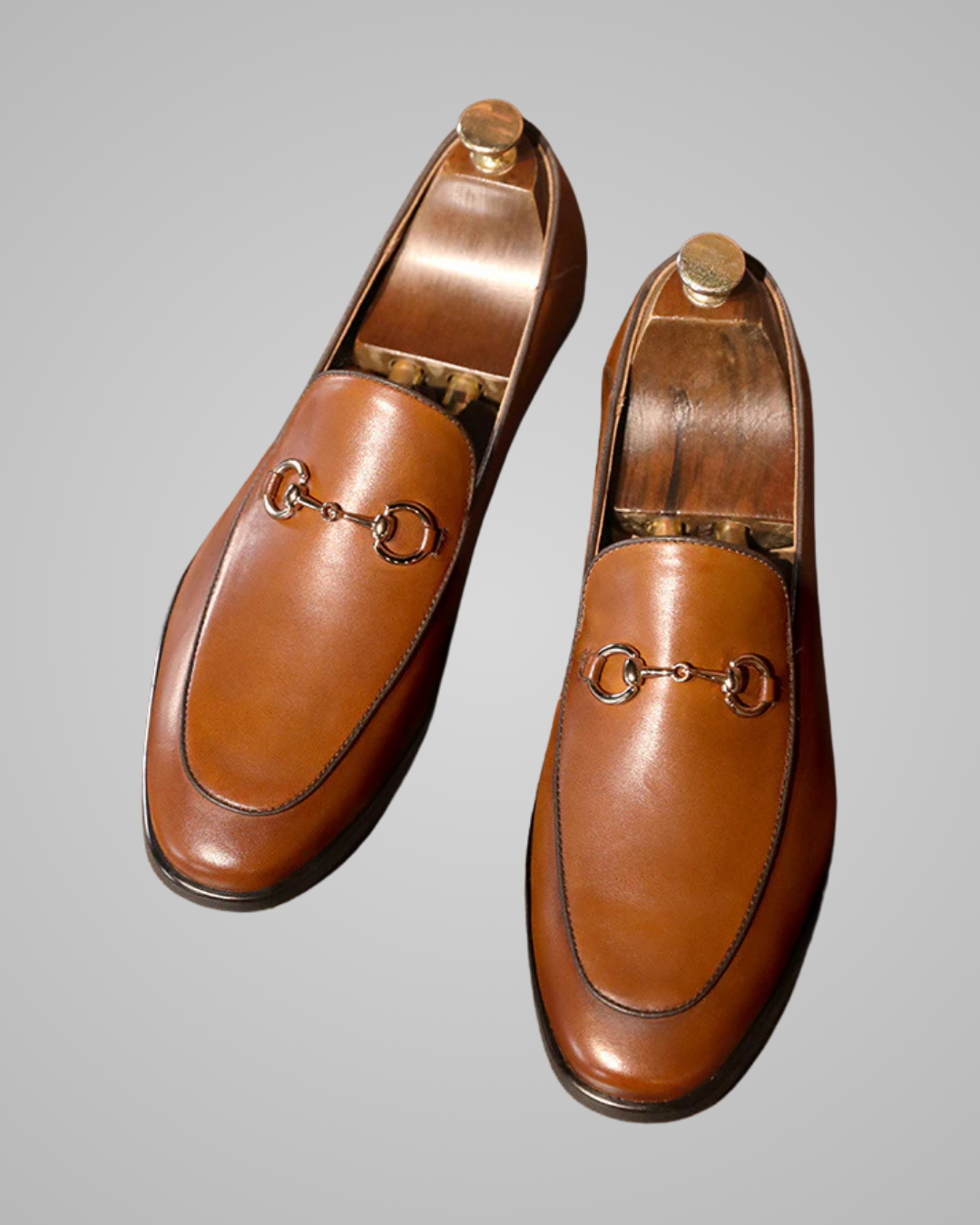 Pair of brown leather loafers with gold hardware on a gray background