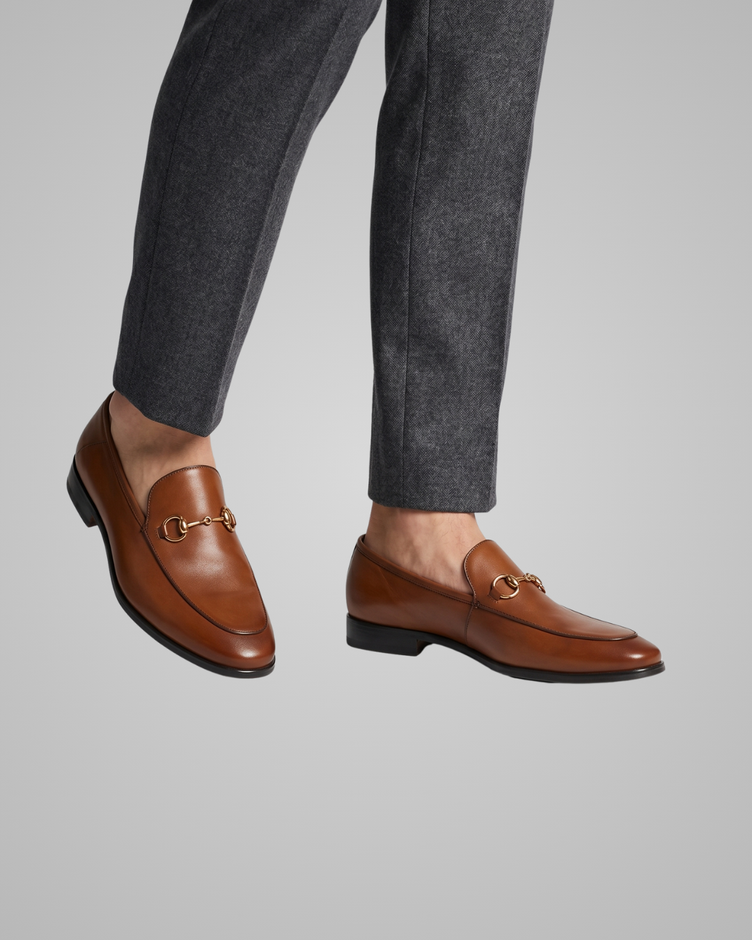 Brown loafers worn with gray pants on a light gray background