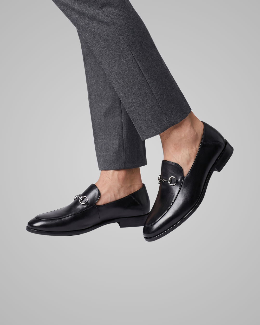 Black loafers worn with gray pants on a gray background
