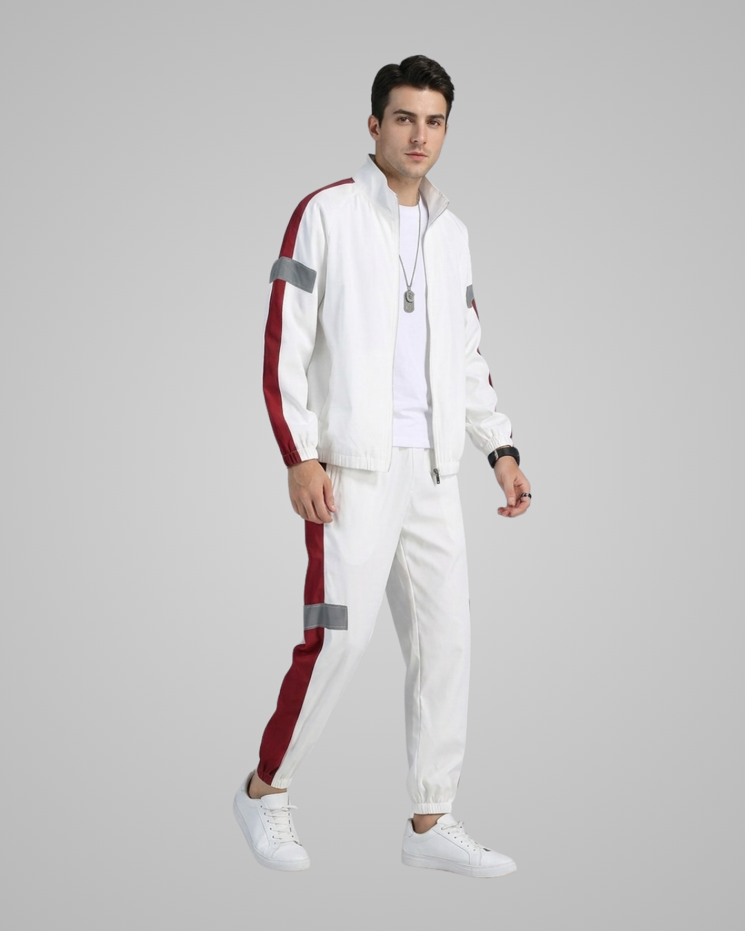 A man modeling a white tracksuit with red and gray reflective stripe details, consisting of a zip-up jacket and matching jogger pants, against a solid gray background.