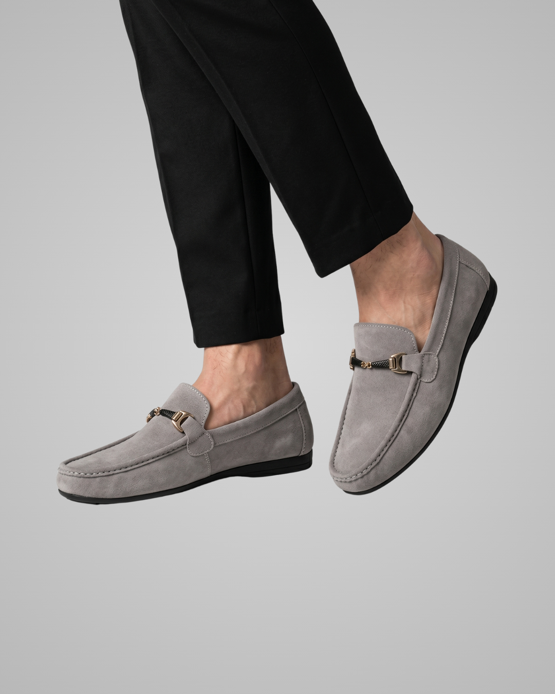 Gray loafers worn with black pants on a gray background