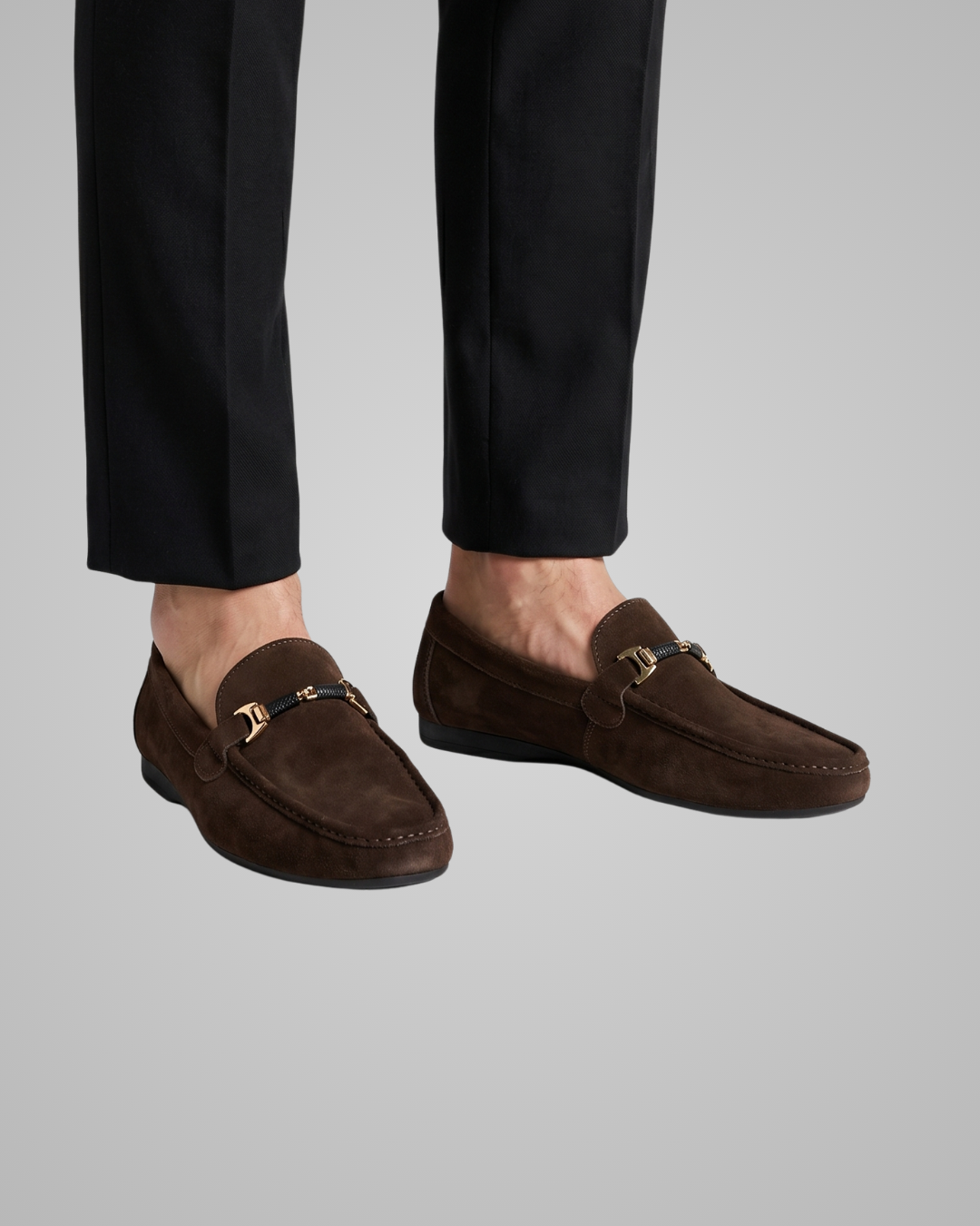 Brown loafers worn with black pants on a light gray background