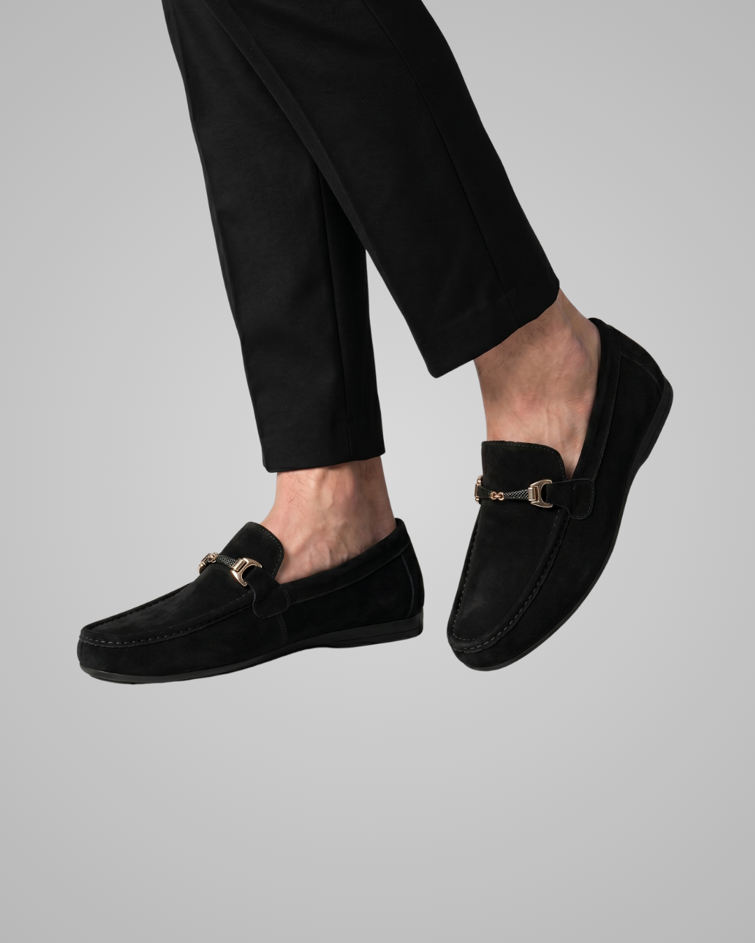 Black loafers worn with black pants on a gray background