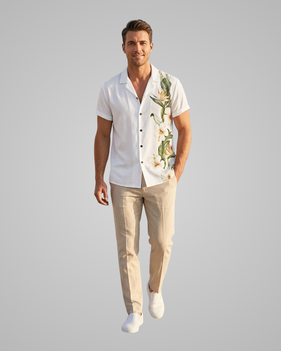 A man modeling a white short-sleeve button-up shirt with a green and white tropical floral print on the right side, paired with beige trousers and white sneakers, against a solid gray background.