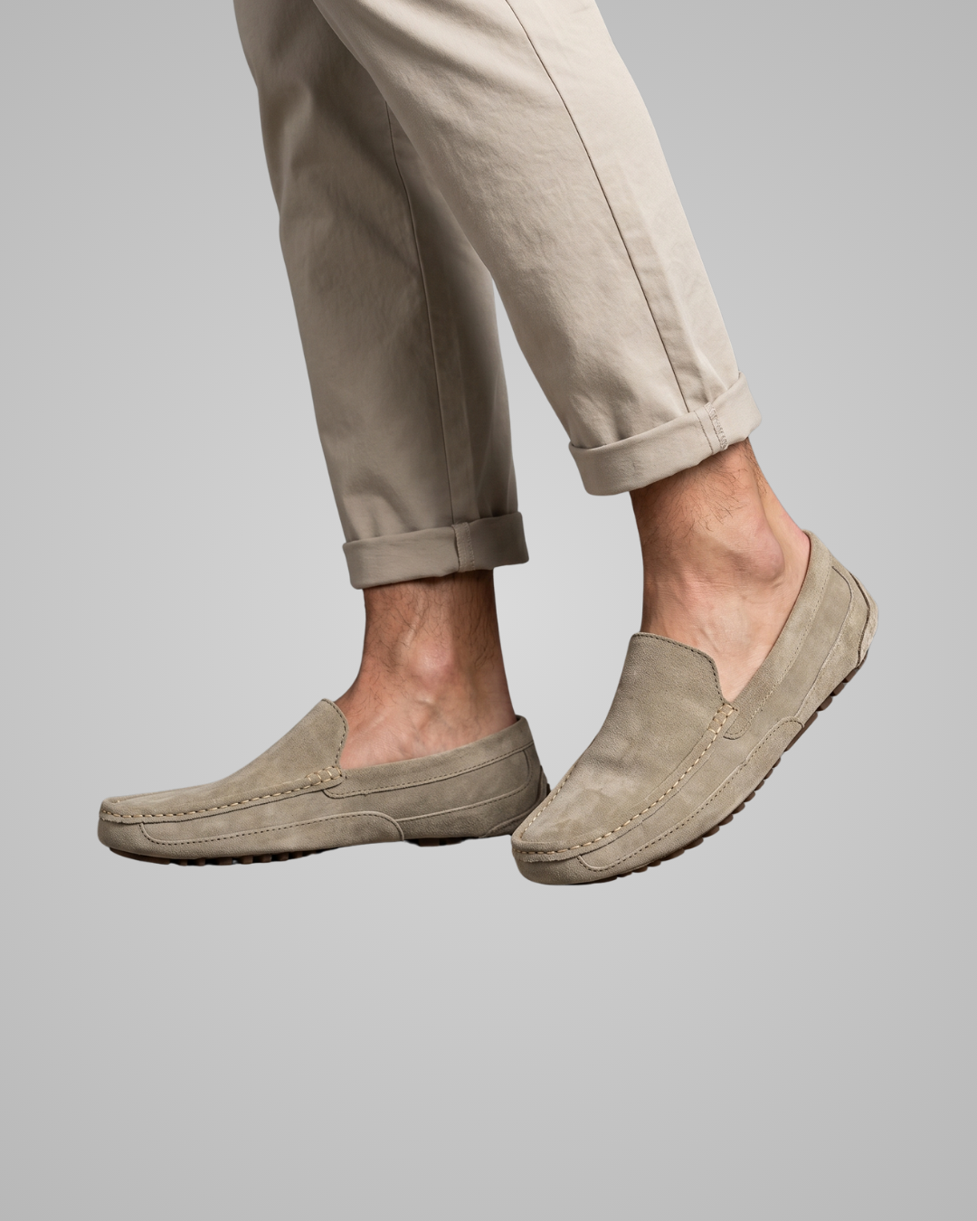 Beige loafers worn with beige pants on a gray background