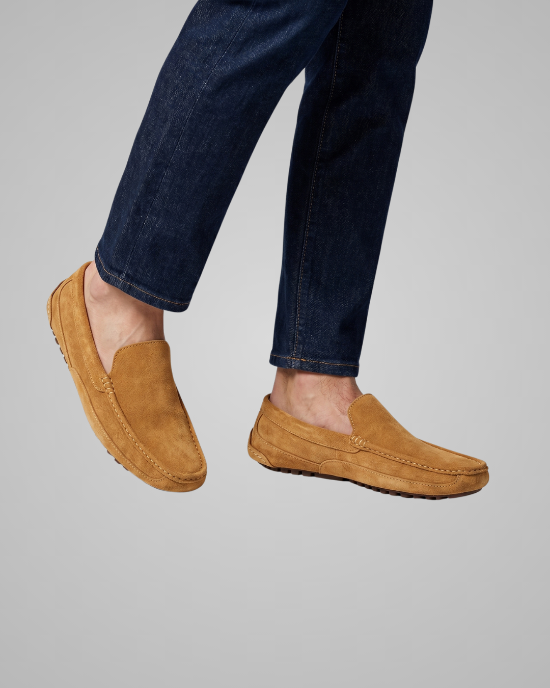 Brown loafers worn with dark jeans on a gray background