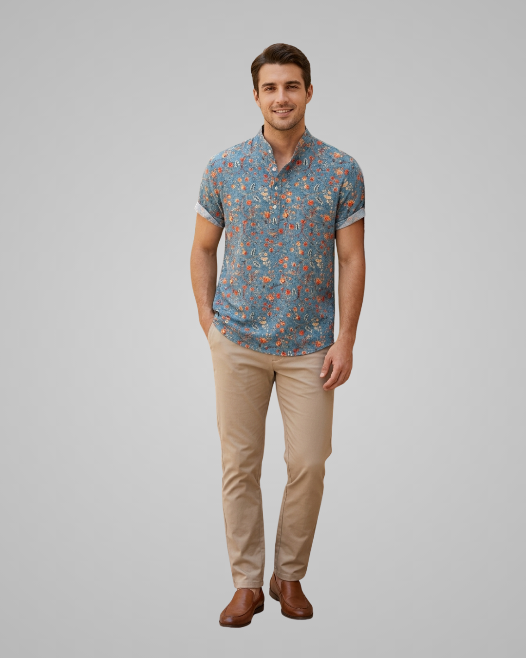 A man modeling a short-sleeve button-up shirt with a blue and orange floral pattern, paired with khaki pants and brown shoes, against a solid gray background.