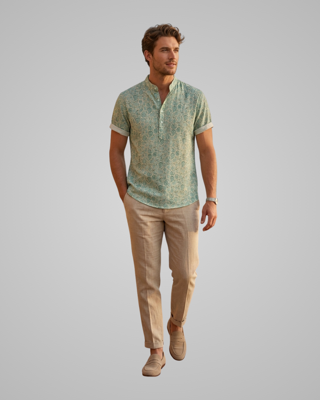 A man modeling a short-sleeve henley shirt with a light green and beige abstract pattern, paired with beige trousers and tan shoes, against a solid gray background.