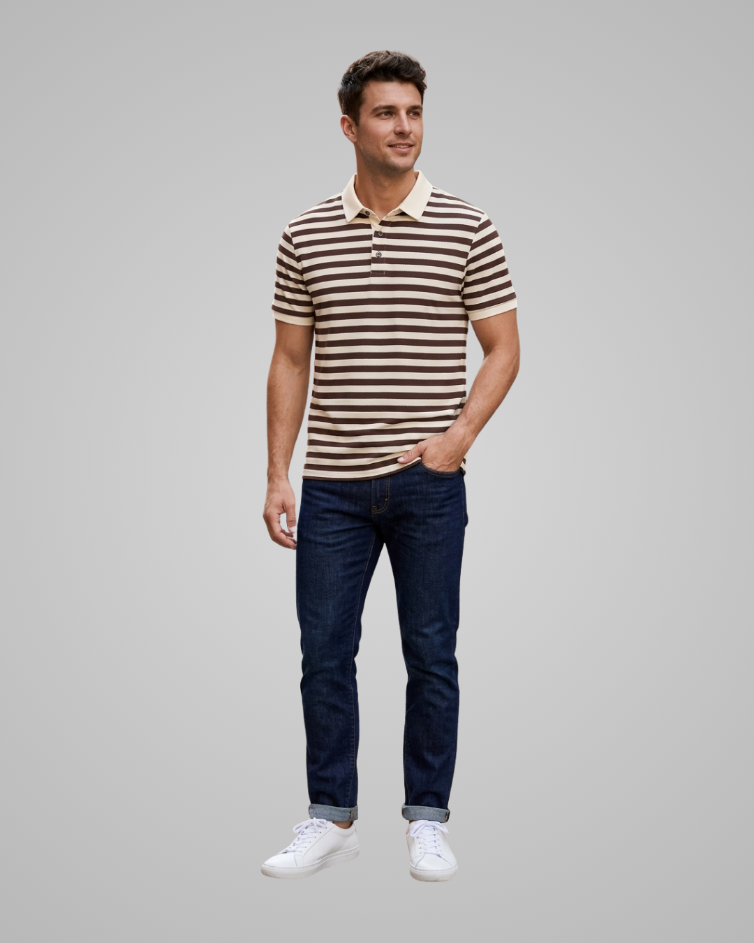 A man modeling a short-sleeve polo shirt with brown and beige horizontal stripes, paired with dark blue jeans and white sneakers, against a solid gray background.