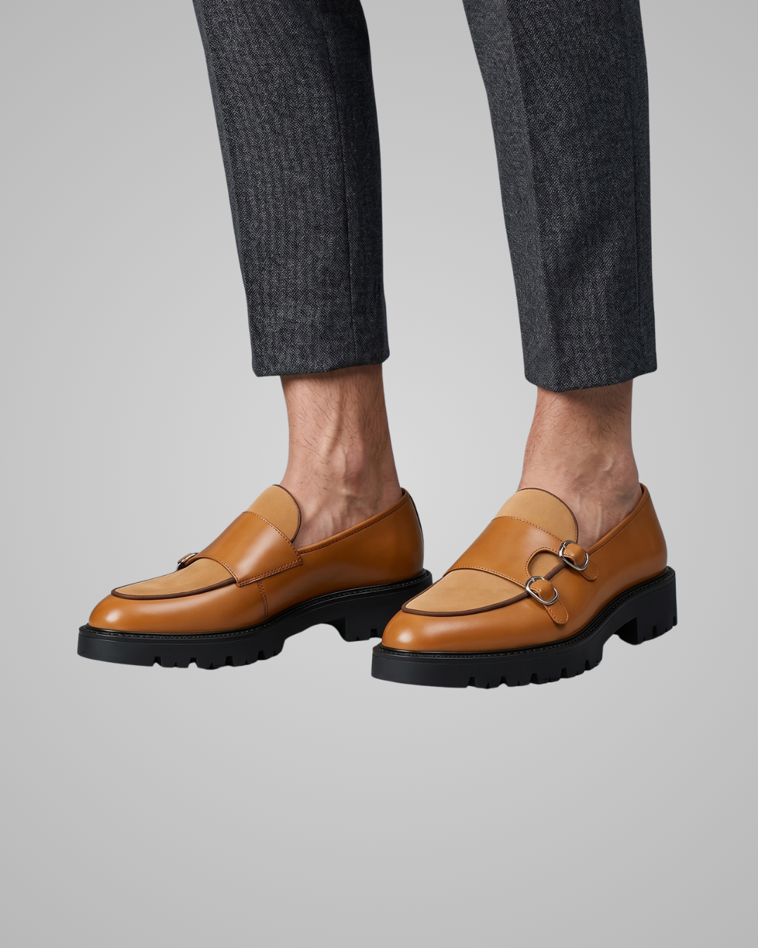 Brown loafers worn with gray pants on a neutral background