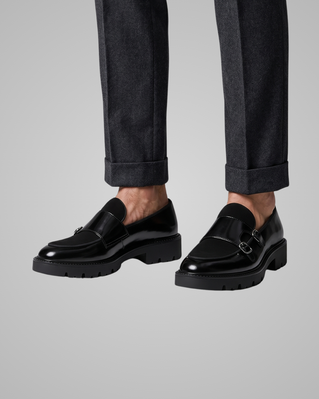 Black leather shoes worn with dark pants on a light gray background
