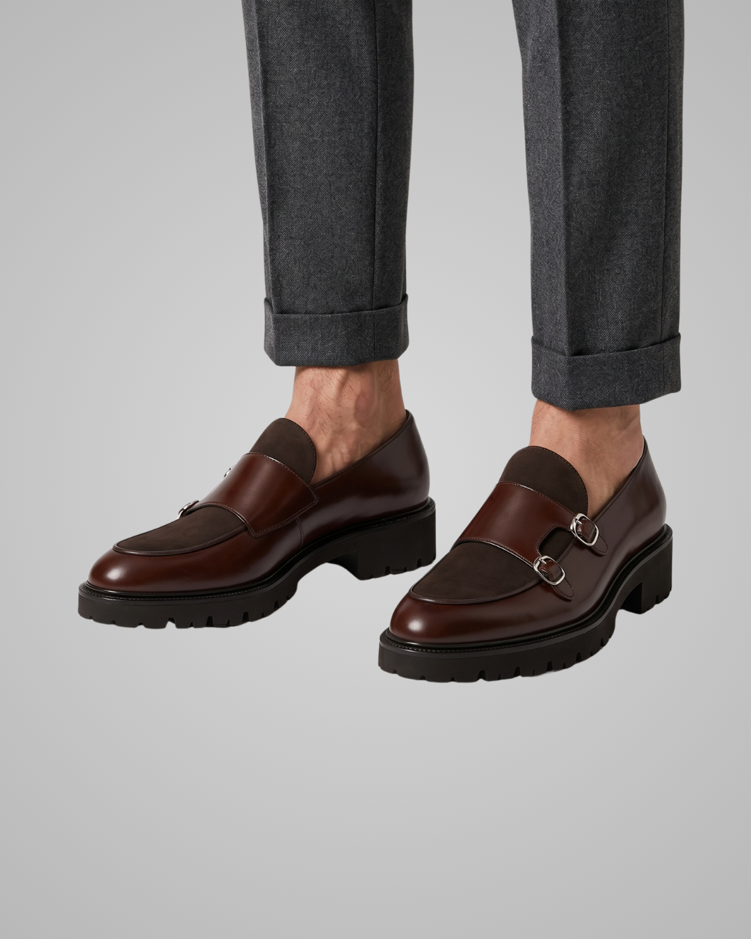 Brown leather shoes with a silver buckle worn with gray pants on a light gray background