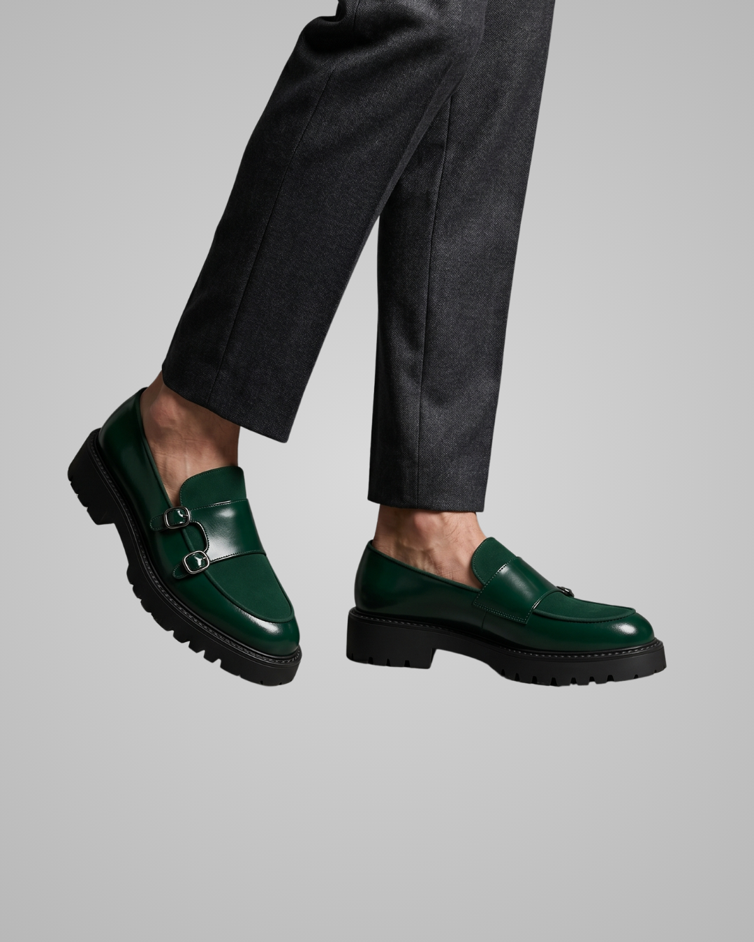 Green loafers worn with black pants on a gray background