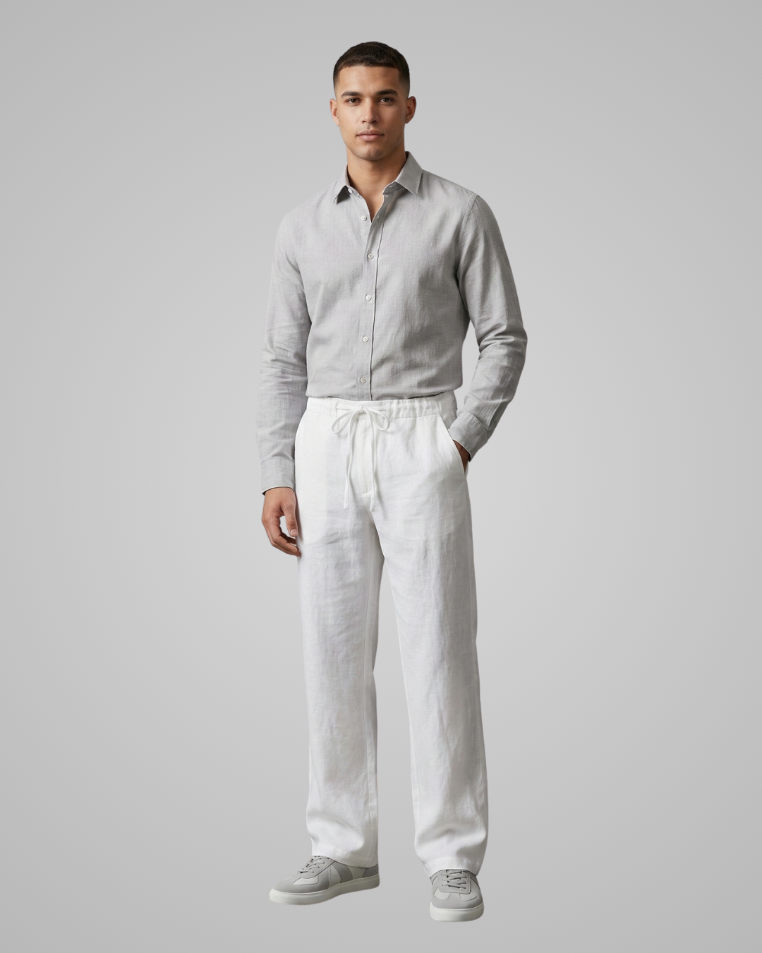 Man wearing a light gray shirt and white pants against a plain background