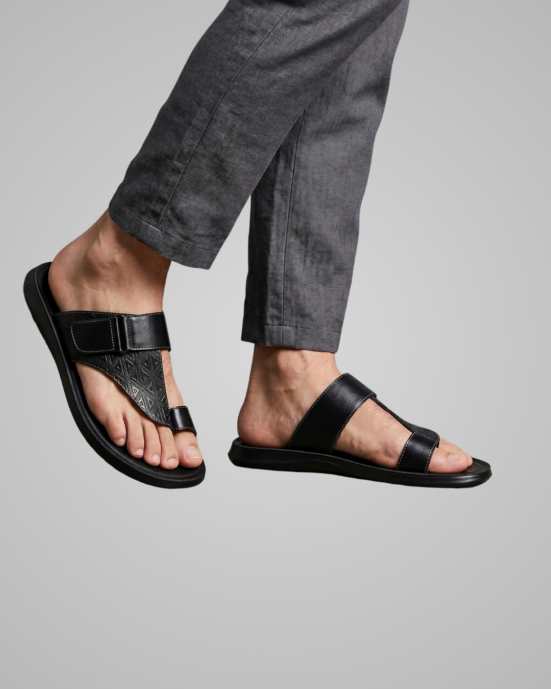 Black sandals worn with gray pants on a plain background