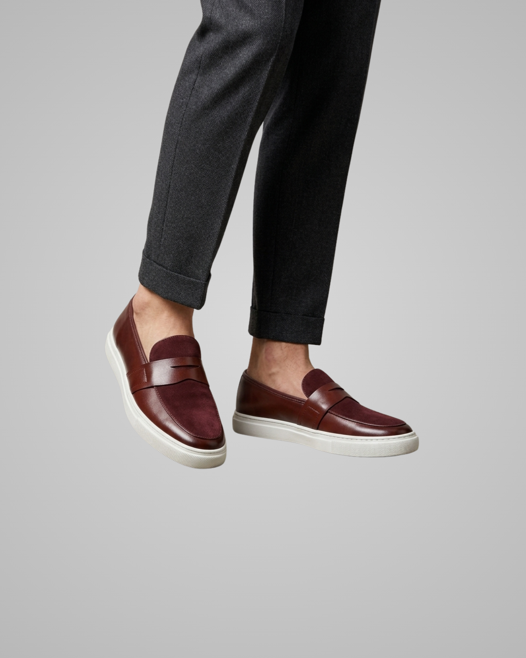 Brown loafers worn with dark trousers on a light gray background